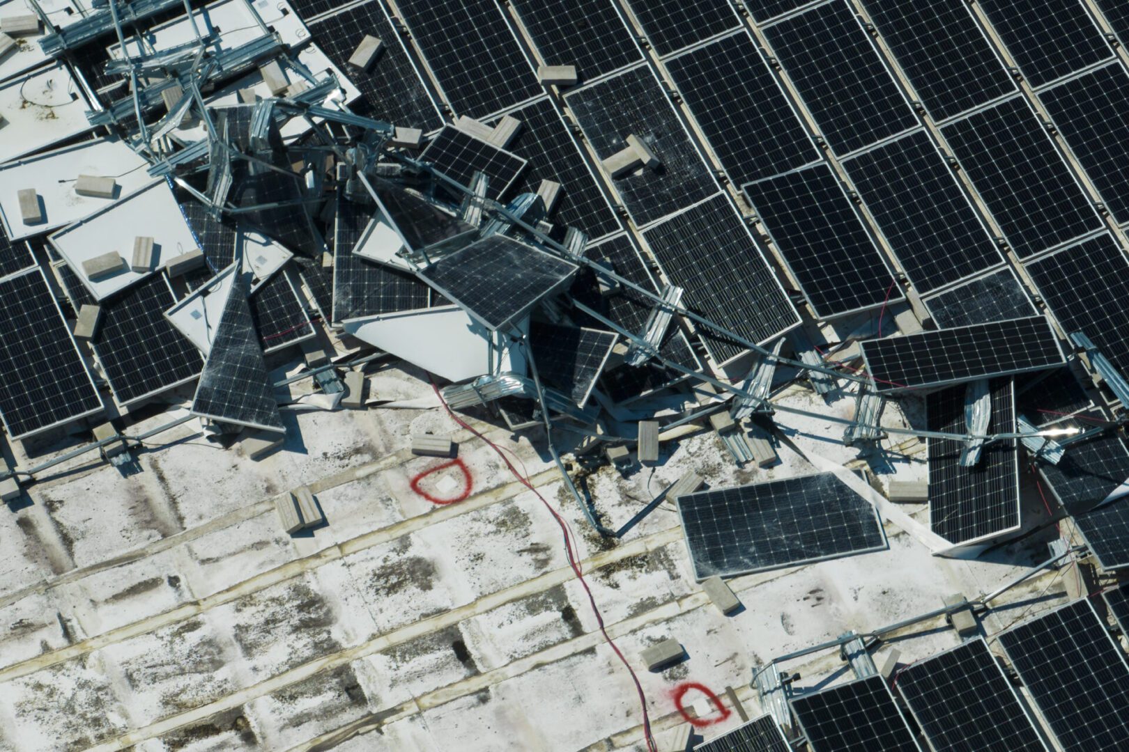 Aerial view of damaged by hurricane wind photovoltaic solar panels mounted on industrial building roof for producing green ecological electricity. Consequences of natural disaster.